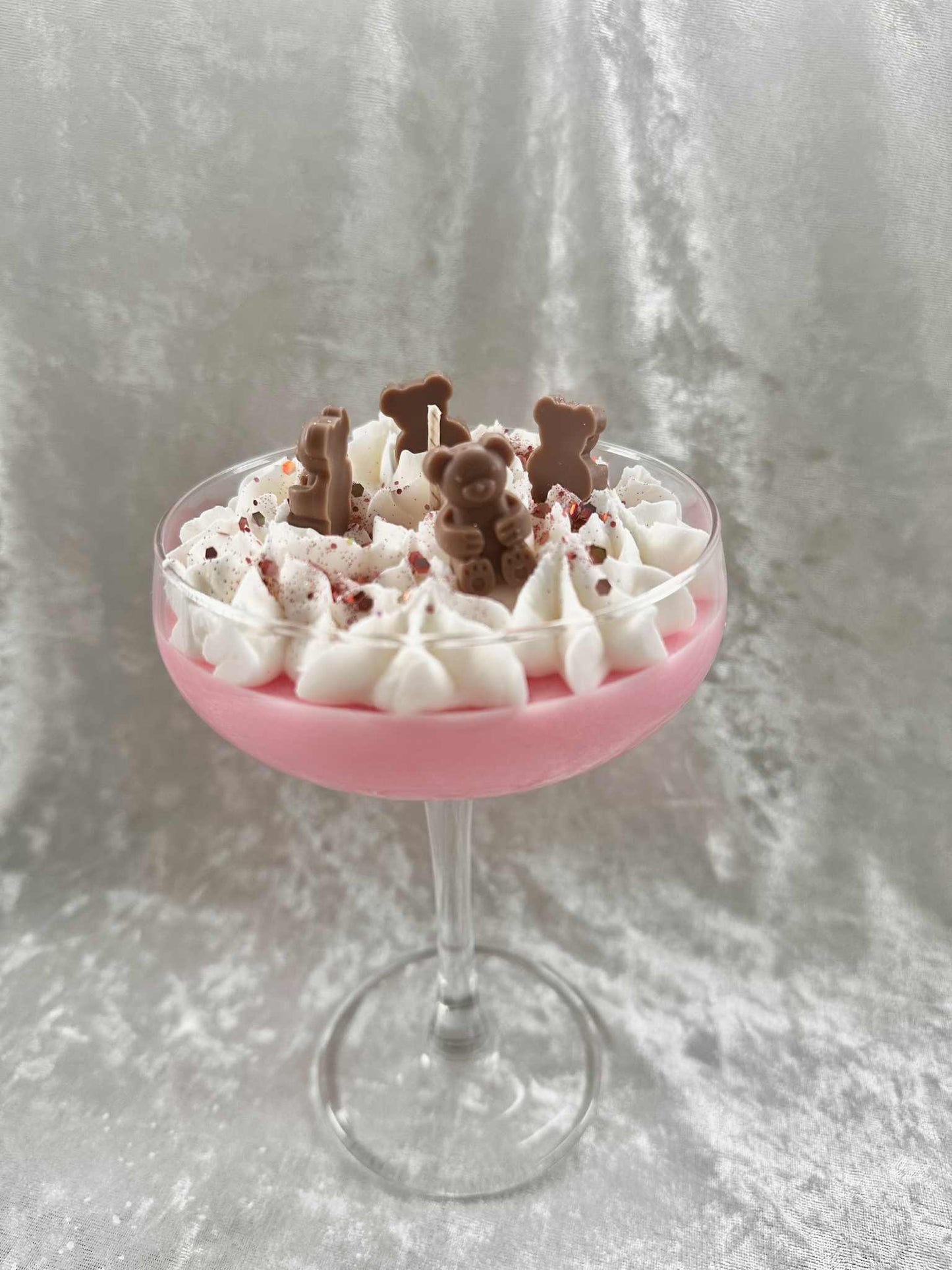 Pink cocktail glass filled with a dessert topped with whipped cream and chocolate bears on a gray background, cocktail candle, home decor, scents, martini