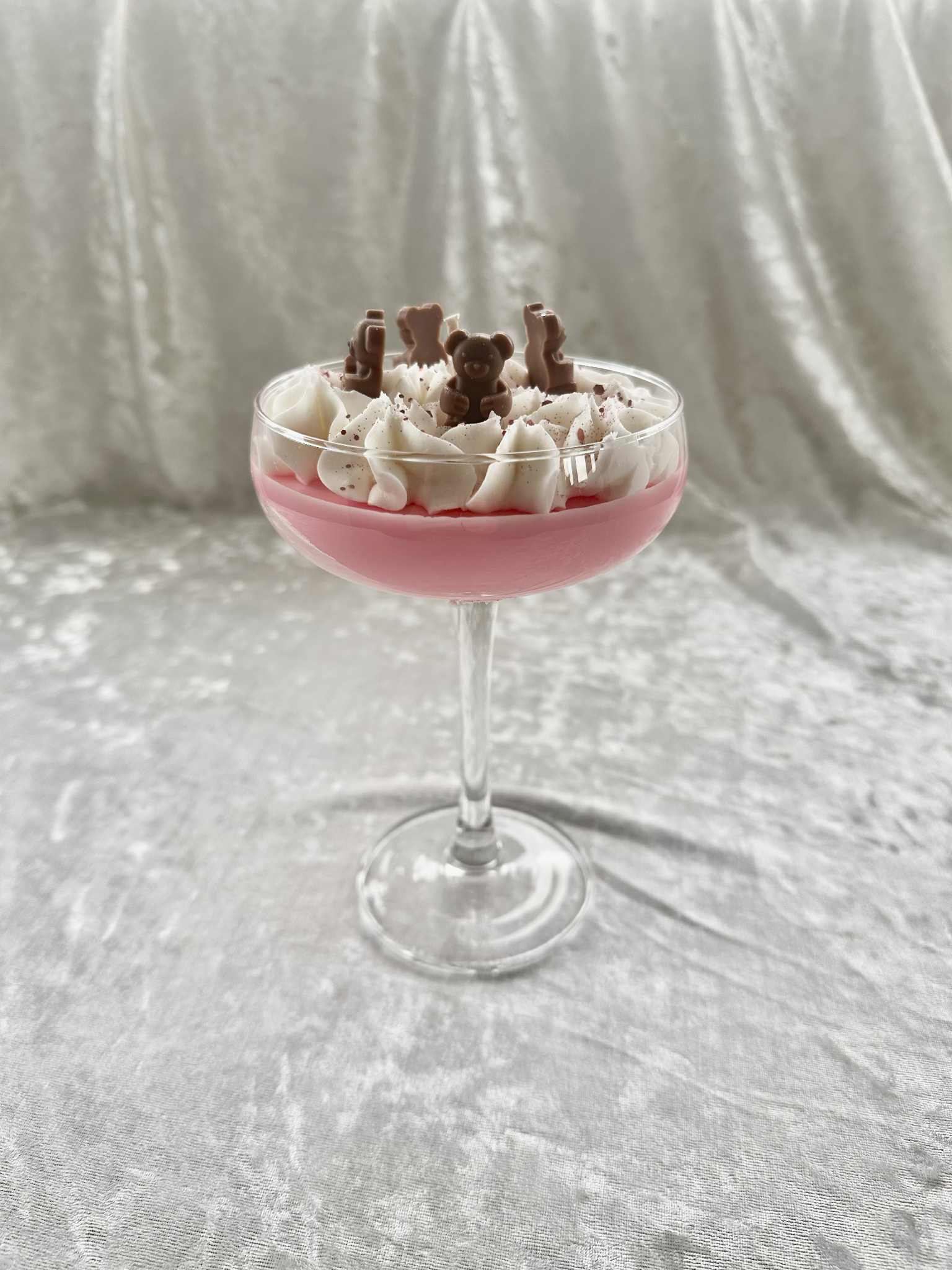Pink cocktail glass filled with a dessert topped with whipped cream and chocolate bears on a gray background, cocktail candle, home decor, scents, martini
