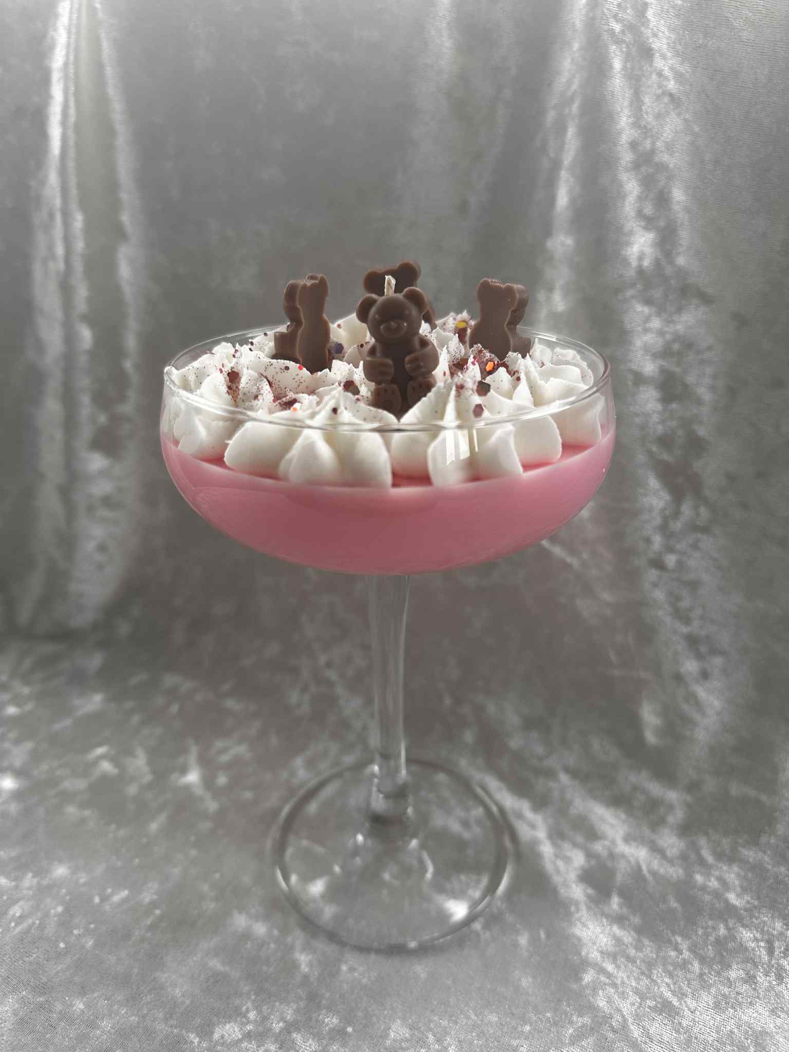 Pink cocktail glass filled with a dessert topped with whipped cream and chocolate bears on a gray background, cocktail candle, home decor, scents, martini